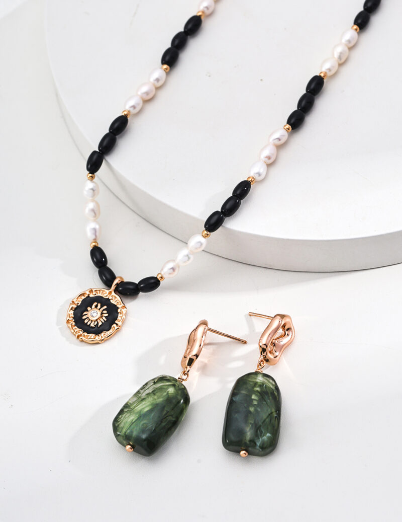 Explore the o_1iac7l2s8gdt10gtrmf1f20196r3, a minimalist jewelry set consisting of a necklace decked with black and white beads, complemented by a gold and black sunburst-patterned pendant, along with matching gold earrings featuring rectangular green stones. The faux amber tones beautifully enhance the display's white background, adding warmth to your style. Elegant pearl jewelry