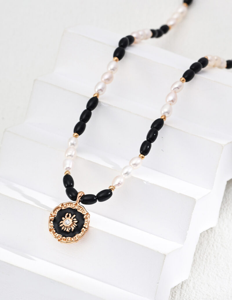 Introducing the o_1iac7vg14r7d1vpg5oi1f6i1lcg2, a captivating Black Onyx necklace adorned with alternating black and white beads, featuring a circular pendant with a central gemstone design, elegantly displayed on staggered white steps. Elegant pearl jewelry